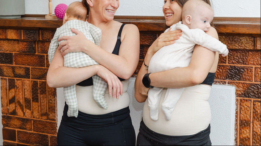 Two postparutm women holding babies in a home setting with a wooden fireplace, wearingabdominal support garment, tubigrip