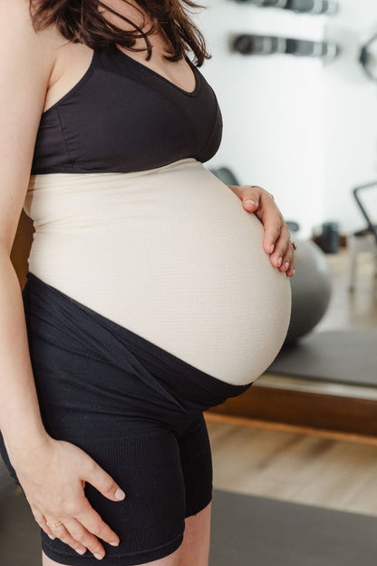 Pregnant person wearing a black top and shorts, holding their belly, wearing abdominal support garment, tubigrip