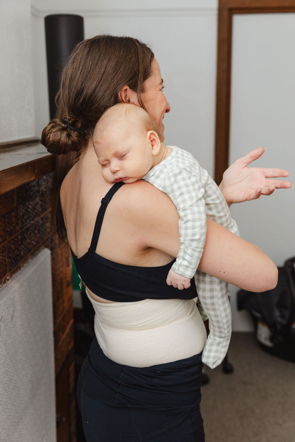 Woman holding a baby, while wearing abdominal support garment, tubigrip in an indoor setting.